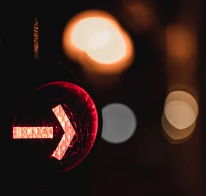 Primo piano di un semaforo rosso con una freccia su uno sfondo sfocato.